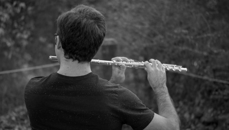 A monochrome image of David Stoeltzing playing the flute, shown from behind