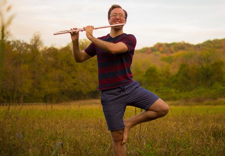 David holding a flute, standing in a field, smiling.